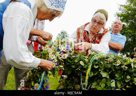 Mariefred, Sweden - June 24, 2016: Two elderly women in traditional costumes attach one of the garlands on the maypole before the rising of the rod at Stock Photo