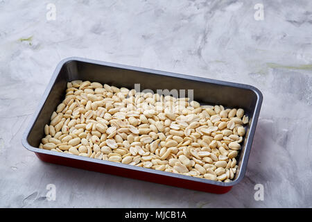 Peeled peanut on baking tray over white textured background, selective focus, shallow depth of field. Ready to bake. Healthful and nutritious snack. D Stock Photo