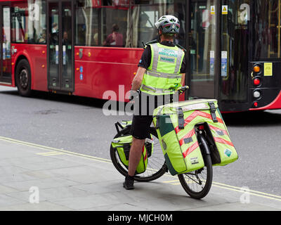 NHS London Ambulance Paramedic on a bicycle in London, UK. 2018. Rear view in front of red London bus. Stock Photo