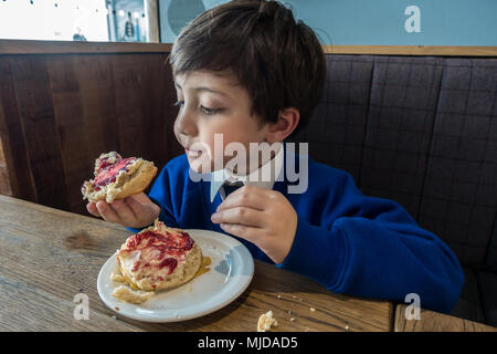 A young boy enjoying a fruit scone topped with clotted cream and raspberry jam. Stock Photo