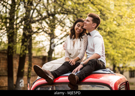 Merry happy young couple sit on the roof of the car. Close-up Stock Photo