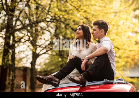 Merry happy young couple sit on the roof of the car. Close-up Stock Photo