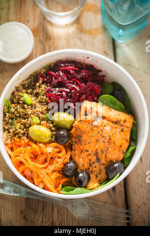 Salmon with spinach leaves, carrots, beetroots, grain edamame salad and black and green olives. Healthy fish and salad protein bowl Stock Photo
