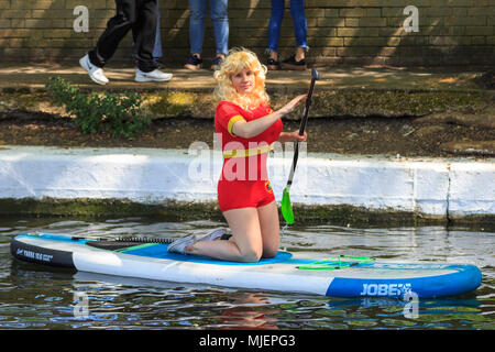 Little Venice, London, 5th May 2018. A young woman dressed as Pamela Anderson from 'Baywatch' tries paddleboarding.  People enjoy the sunny day as colourfully decorated narrowboats fill the Little Venice 'Pool', a basin on the Grand Union canal in Little Venice for the IWA Canalway Cavalcade waterways festival, which celebrates boating on the British waterways.Over 50 boats taking part in a pagent and competition, and many more lining the banks of the canal for the festival from May 5-7th. Credit: Imageplotter News and Sports/Alamy Live News Stock Photo