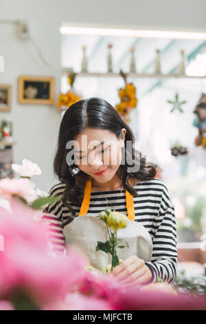 Young beautiful asian girl florist taking care of flowers at workplace. Stock Photo