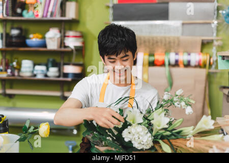 Happy asian male florist using laptop at counter in flower shop Stock Photo