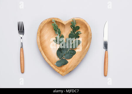 Wooden plate in shape of heart, table knife and fork on white background. Stock Photo