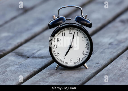Black alarm clock with white dial on a table showsa few minutes past seven. Stock Photo