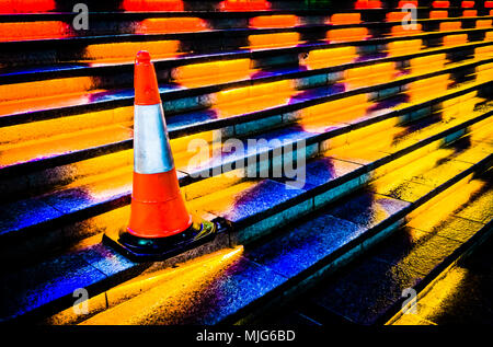 Isolated traffic cone on stair case with colorful yellow and orange lightings. Stock Photo