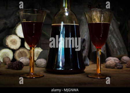 Red Wine Vintage Bottle and Glasses Resting On Wooden Table Against Christmas Background With Wood logs and Pine Branches Stock Photo