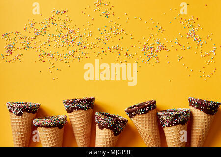 Ice cream cone with colorful sprinkles on yellow background.