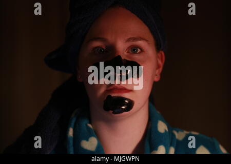 Women with a charcoal mask on as part of her beauty regime. This is a caucasian women who is aged 20 to 25 years old and is of British descent. Stock Photo