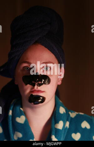 Women with a charcoal mask on as part of her beauty regime. This is a caucasian women who is aged 20 to 25 years old and is of British descent. Stock Photo