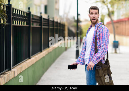 Young bearded man surprised in urban background. Tourist wearing casual clothes. Lifestyle concept. Stock Photo