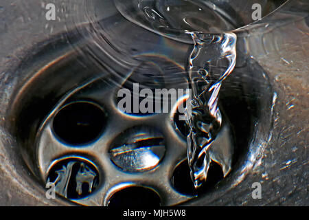 Water spiralling down the plughole in a stainless steel sink. Stock Photo