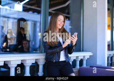 Gladden girl typing by smartphone at street cafe. Stock Photo