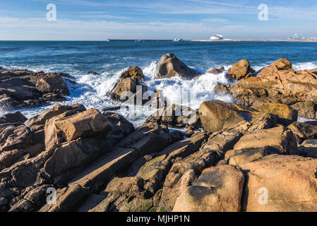 Rocks on the beach in Nevogilde civil parish of Porto, Portugal. Port of Leixoes Cruise Terminal building on background Stock Photo