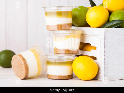Plastic cup with lemon lime cream and biscuit dessert with raw lemons in white wooden box Stock Photo