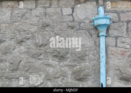 Old blue metal drainpipe with flaky paint on a grey stone wall. Background texture Stock Photo