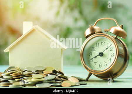 stacked of coins to save for house with alarm clock on wood table with sunlight background, concept as investment, finance, account and stock market Stock Photo