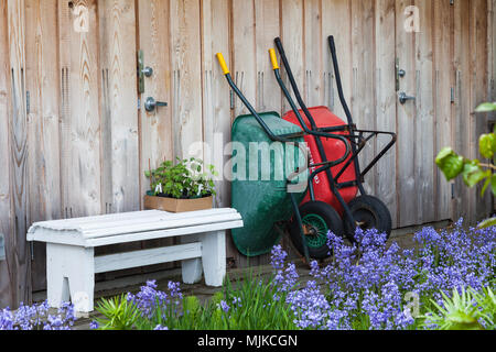 Wheel barrows against a garden shed by a flower bed Stock Photo