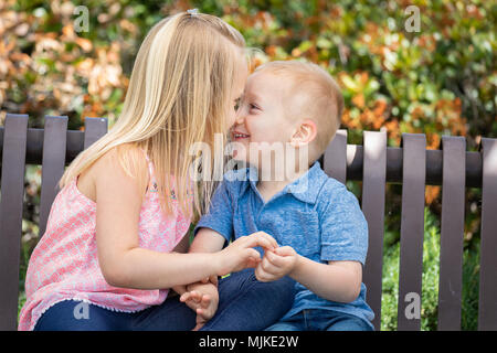 Young Sister and Brother Having Fun On The Bench At The Park. Stock Photo