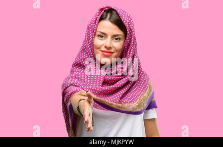 Young arab woman wearing hijab holds hands welcoming in handshake pose, expressing trust and success concept, greeting Stock Photo