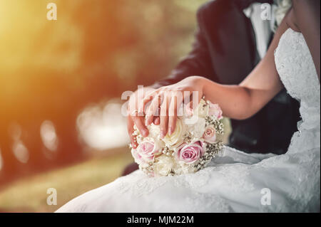 Wedding day. Bride and the groom sitting on a bench in the park. Bouquet in focus. Stock Photo