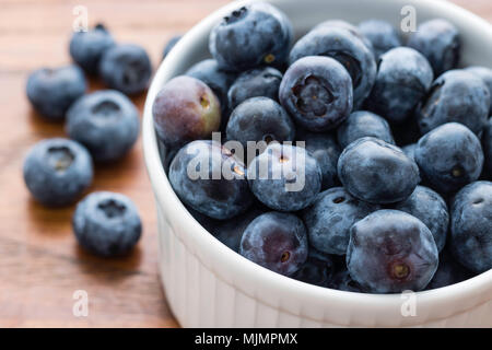 Small White Bowl filled with Fresh Blueberries, Six Blueberries on the left, Wooden Board Background, Healthy Eating Concept Stock Photo