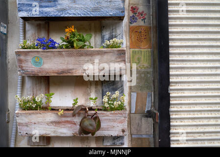 Wooden rectangular boxes with orange flowers on the wall of the house, decorated with multicolored tiles, to the right white roller shutters, urban ba Stock Photo