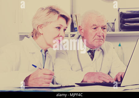 Mature male doctor and female nurse working effectively in office Stock Photo