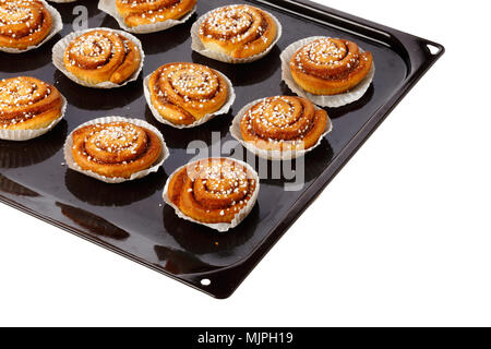 Cinnamon buns in tins of greaseproof paper on a baking tray on white. Stock Photo