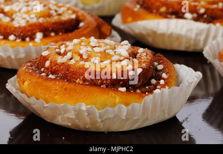 Close-up of cinnamon buns in tins of greaseproof paper on a baking tray. Stock Photo