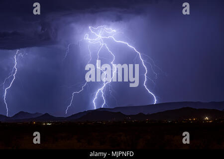 Bright lightning bolts illuminate the sky above Carefree, Arizona as they strike a mountain during a summer thunderstorm Stock Photo