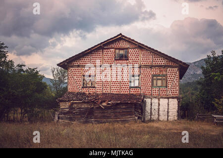 A rustic, abandoned house in a rural setting with a red-and-white checkered facade, old wooden beams, and a decaying roof, Stock Photo