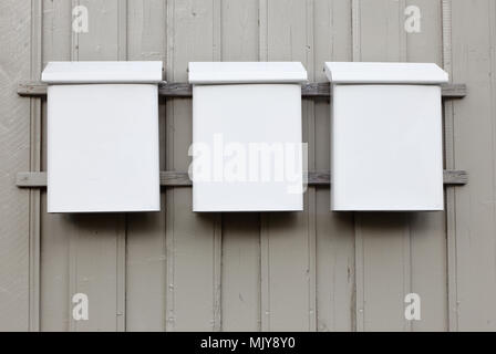 Three white mailboxes of sheet metal mounted on a gray wooden wall. Stock Photo