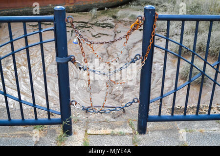 The ends of two blue fence rails with the posts connected by blue and orange chains Stock Photo