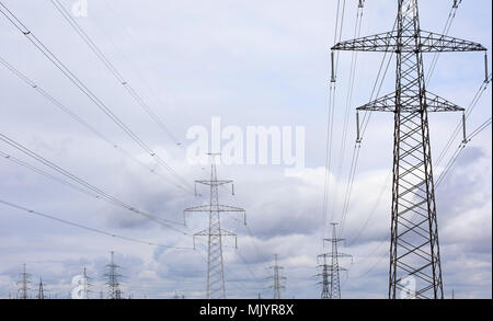 High voltage lines and power pylons on dramatic sky with grey clouds Stock Photo