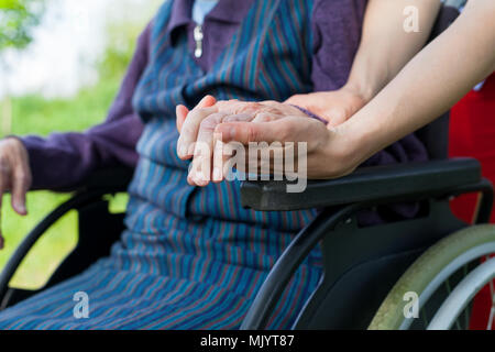 Close up picture of carer holding elderly woman's shaking hands, sitting in a wheelchair - Parkinson disease Stock Photo