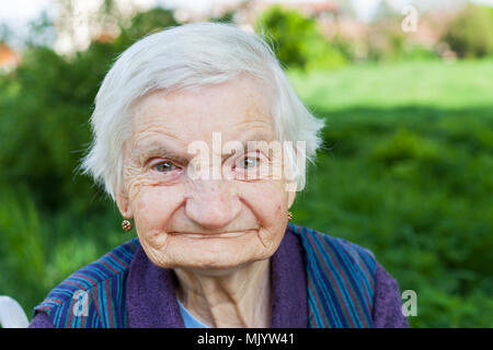 Close up portrait of smiling elderly woman suffering from dementia disease, outdoor Stock Photo