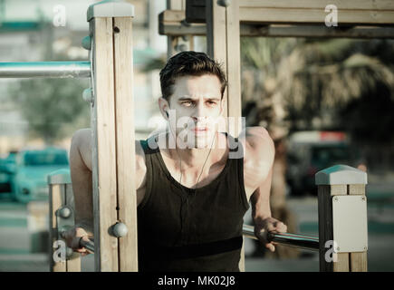 Happy cheerful  strong man doing parallel bar dips to music on sports ground on beach Stock Photo