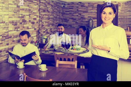 Young female waiter welcoming guests to country restaurant Stock Photo