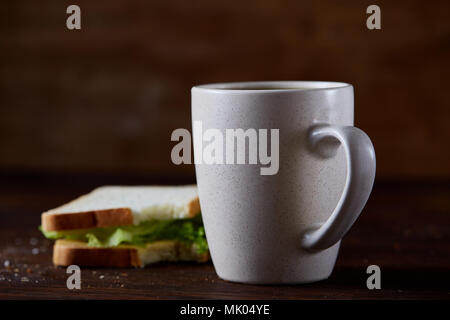 Breakfast table with fresh cheese and lettuce sandwich and black coffee in white ceramic mug on rustic wooden background, close-up, selective focus. B Stock Photo