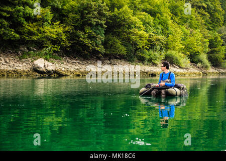 Fisherman sitting in bellyboat, waiting for contact with trout and watching the shoreline, lake near Jesenice, Slovenia. Still water fly fishing. Stock Photo