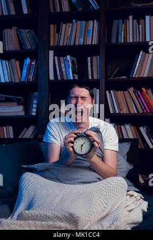 Photo of screaming man with insomnia sitting in bed with alarm clock Stock Photo