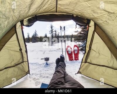 Cooking in front of tent in snow.  Hiker camping in winter mountains.  Man cooking food with portable gas cooker and light dishes. Burning gas stove a Stock Photo