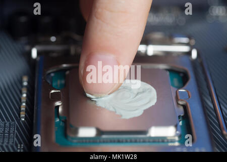 Applying thermal paste with finger in CPU on motherboard close up Stock Photo