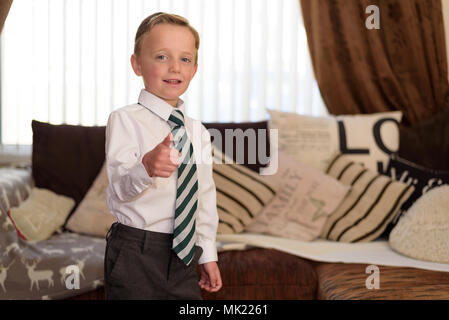 Young boy dressed in new uniform and ready for school, whilst holding thumb up Stock Photo