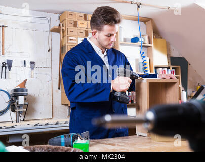Young smiling man using drilling machine to make drawer at workshop Stock Photo
