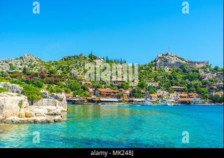 The view on scenic Kalekoy village with lush gardens, small cottages, yachts and Simena Castle from waters of Kekova Bay, Turkey. Stock Photo